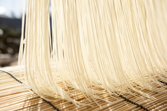 Thin white noodles drying on a bamboo blind in soft sunlight.