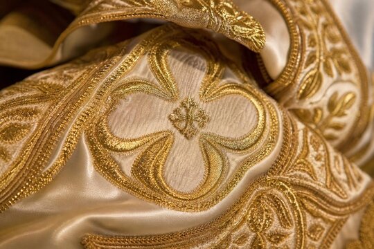 Extreme close-up of intricate gold embroidery on heavy liturgical silk fabric.