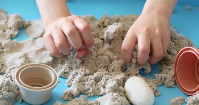 Children activity with kinetic sand for motor and sensory development. Toddler play therapy with colorful toys on wooden sandbox.
