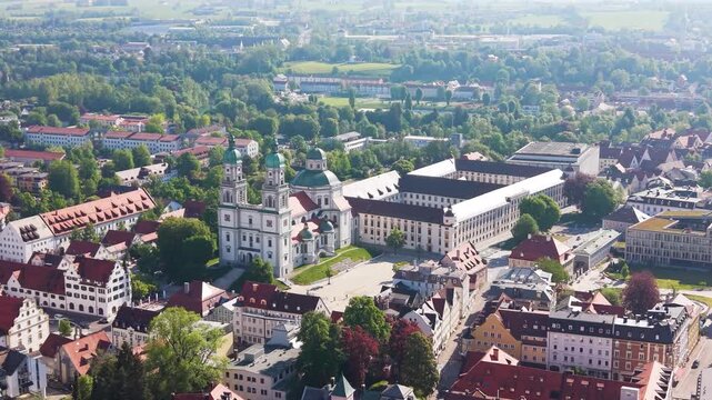 Detailed push in drone shot of Kempten in Bavaria featuring the Basilica of Saint Lorenz surrounded by historic buildings and a green urban landscape under bright daylight, UHD.