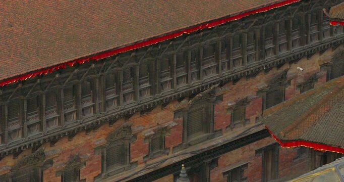 Drone moves sideways in a smooth lateral tracking shot, passing closely along the intricately carved wooden windows of the historic 55-Window Palace facade in Bhaktapur Darbar Square, Nepal.
