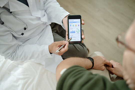 Senior patient visiting doctor in clinic, reviewing glucose monitoring app on smartphone during consultation. Supporting diabetes care, telehealth promotion, patient education marketing