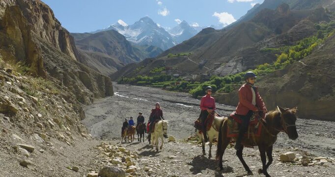 A fixed, eye-level aerial shot captures riders passing the camera in Mustang, Nepal, showcasing the dramatic mountain, hills, and rough terrain.