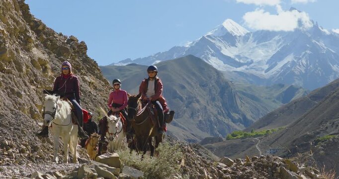 A stable, low-perspective aerial composition keeps the riders as the central focus as they journey through Mustang, Nepal, traveling along a rugged hillside and massive hills.