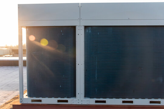 A modern industrial HVAC chiller system and large air conditioning condenser units installed on a flat commercial building rooftop. 