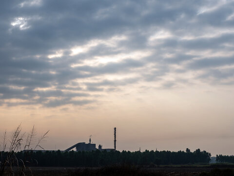 Factories and tall smokestacks stand alone amidst agricultural and wasteland areas