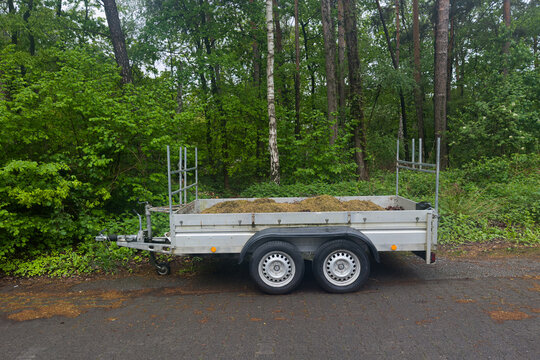Trailer with grass and leaves in a wooded area during daytime
