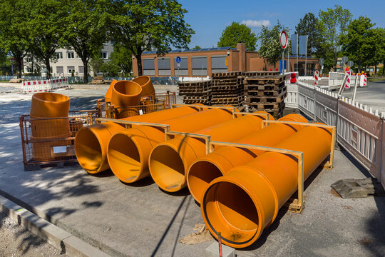 Several orange pipes are arranged on the ground at a construction site