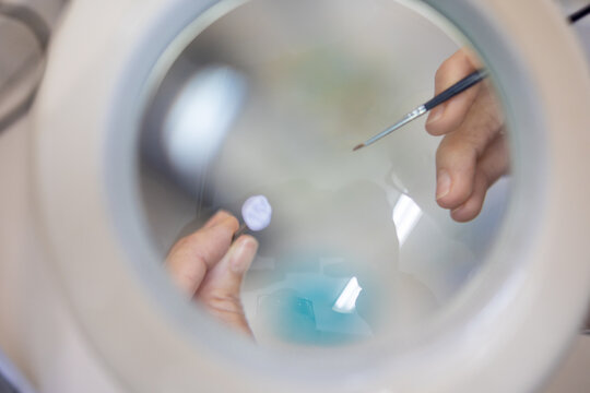 Dental Technician Painting Ceramic Crown Under Magnifying Lamp