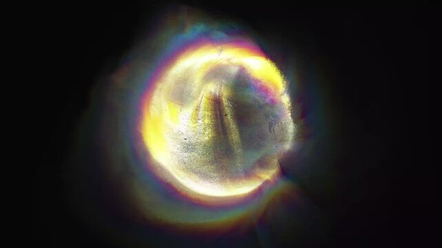 Abstract golden iridescent glowing ball highlighted on a black background. Abstract sphere of liquid gold with iridescent light. Ethereal holographic ball of warm light.