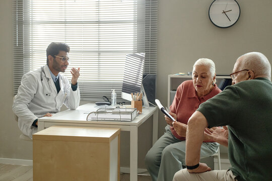 Senior couple visiting doctor in clinic, discussing medical document during consultation and treatment planning. Ideal for healthcare access, patient care, insurance marketing