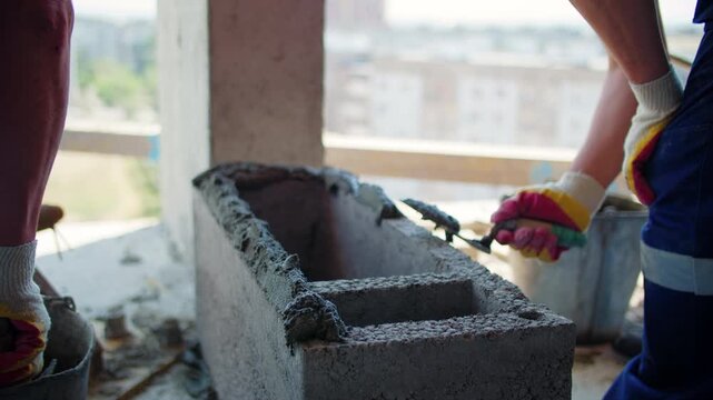 Workers applying mortar to hollow concrete block indoors