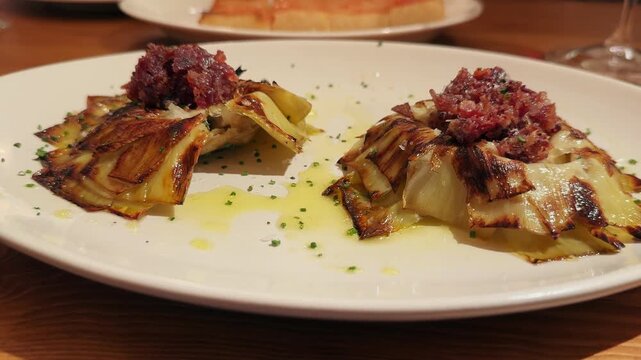 A close-up of fried artichoke blossoms served on a plate, drizzled with olive oil and topped with crispy ham. Authentic Mediterranean cuisine.