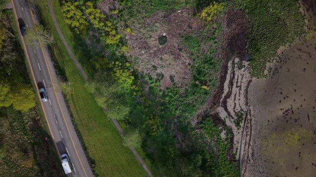 Top-down aerial drone shot showing cars passing each other on the A83 road along the tidal shoreline at the end of Loch Long.