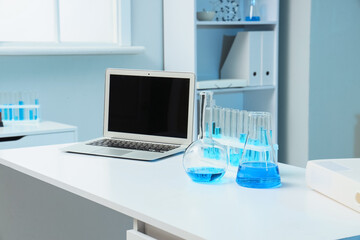 Fototapeta premium Modern laboratory workspace with laptop and blue liquid in glassware, scientific research and education environment