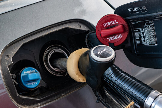 Refueling car with diesel fuel pump nozzle at gas station close up.Diesel fuel nozzle inside car tank neck next to blue AdBlue cap.