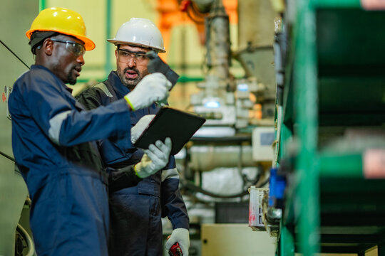 Factory workers reviewing technical information on digital tablet during equipment maintenance operation. Skilled technicians collaborating on troubleshooting, quality control.