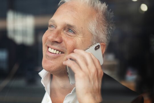 Smiling man talking on a smartphone, wearing a white shirt, indoors.