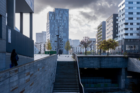 Urban architecture opens around concrete stairs and railing, where a modern building, plaza, facade, skyline, exterior and shadow frame the access