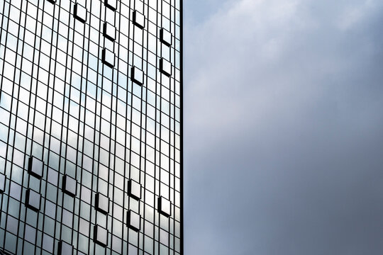 Beside open sky, a glass skyscraper facade rises with grid windows, modern architecture, reflections, office tower and vertical exterior lines