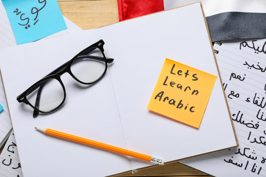Arabic language learning materials with notebook, pencil, glasses, and "lets learn arabic" sticky note