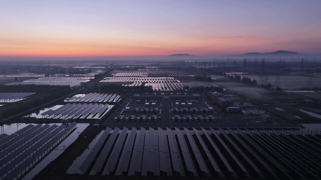 Aerial view of photovoltaic power station at sunrise with orderly solar arrays and misty farmland