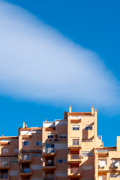 Apartment rooftops and balconies sit below a sweeping cloud in Benidorm, where blue sky and residential architecture shape the highrise exterior