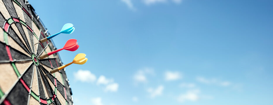 Dart in bullseye of dartboard with blue sky background  hitting target, goal and success