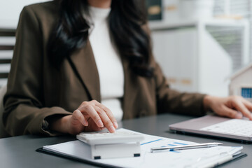 Fototapeta premium Businesswoman using a calculator to analyze financial charts and report at office desk with a laptop, accounting, calculating tax, or planning budget