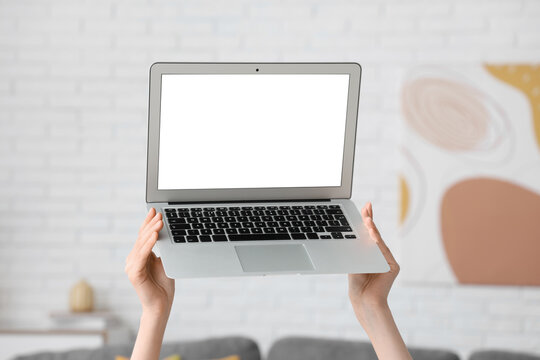 Young woman holding modern laptop with blank screen at home
