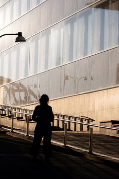 A silhouette of a person walking on a ramp in Stockholm, where urban architecture, glass facade and shadows stretch along the passage