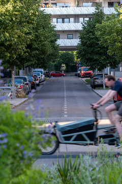 In Vienna, people and bicycles appear on a street where greenery, urban neighborhood architecture and parked cars frame daily city depth