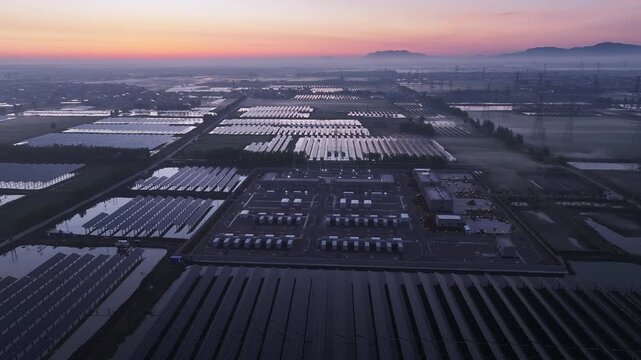 Aerial view of a large-scale photovoltaic power station at sunrise with solar panels and industrial facilities