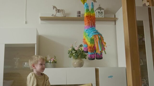 Young boy hitting a colorful birthday pi&ntilde;ata with a toy bat as a tiny piece of paper flies off