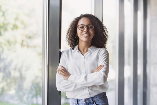 Young businesswoman portrait. Self confident young woman worker with crossed hands smiling at office. People, casual business person, self confidence, leadership