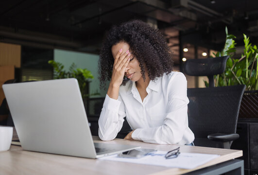 Stressed business woman sitting at office workplace. Tired and overworked business woman. Young exhausted girl during her work using laptop computer