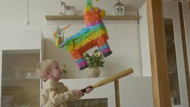 Young boy swinging a w toy bat to hit a colorful hanging donkey pi&ntilde;ata at a birthday party