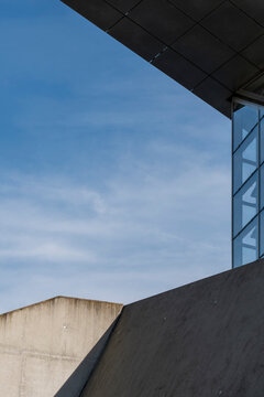 Concrete wall meets blue sky beneath modern architecture as a glass corner and exterior shadow create minimal urban geometry in depth