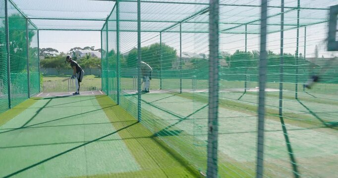 Practicing batting male teammates wearing helmets in net cages at cricket yard holding bats