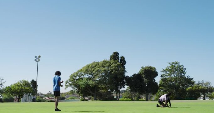 Black male in blue shirt sprinting to catch ball on field after toss, third teammate joining