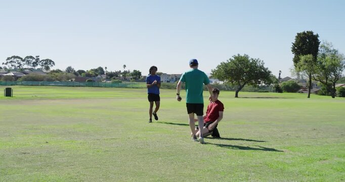 Diverse male teammates on field, one teammate diving to intercept disc being thrown