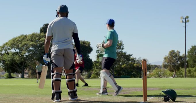 Teenage wicketkeeper catching and returning ball at stumps at cricket oval, bowler bowling