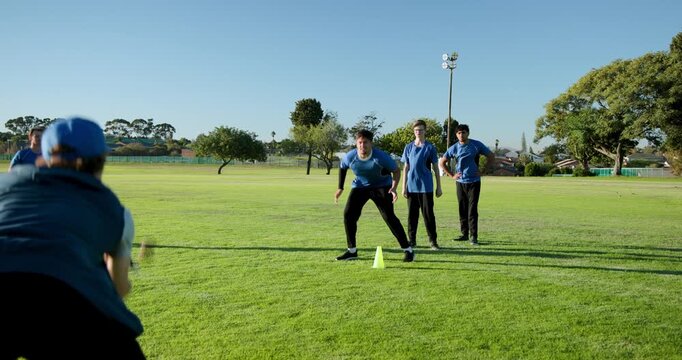 Diverse male team practicing diving catch drill on field with thrower tossing ball at cone