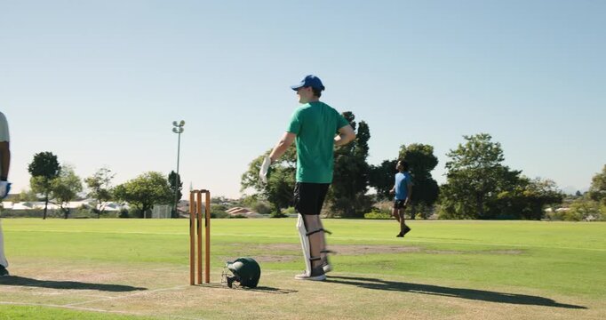 Stumps standing with green helmet lying on cricket pitch, batsman standing under floodlights