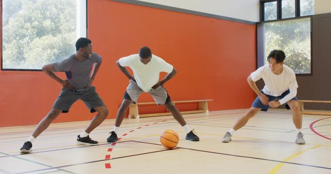 Placing hands on hips diverse male athletes warming up with lunges, stretches on basketball court