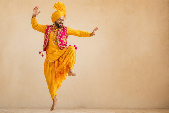 Happy Punjabi Man Dancing Bhangra on Baisakhi Harvest Festival, Cheerful Indian Dancer in Traditional Yellow Costume and Turban
