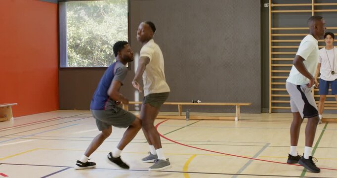 Coach blowing whistle directing african american men practicing defense skills with basketball