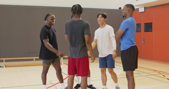 Diverse male team shaking hands then planning positions as coach tapping stopwatch on court