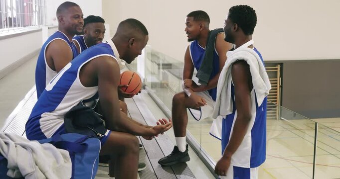 Diverse basketball partners resting on court sideline planning next play while passing basketball
