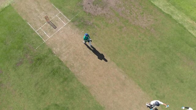 African american bowler nearing crease bowling ball at white batsman raising bat striking ball